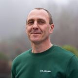 Lächelnder Mann in einem grünen Pullover mit der Aufschrift 'DR. KELLER', der vertrauenswürdig und freundlich wirkt.