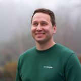 Lächelnder Mann in einem grünen Pullover mit der Aufschrift 'DR. KELLER', der vertrauenswürdig und freundlich wirkt.