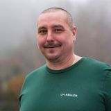 Lächelnder Mann in einem grünen Pullover mit der Aufschrift 'DR. KELLER', der vertrauenswürdig und freundlich wirkt.