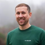 Lächelnder Mann in einem grünen Pullover mit der Aufschrift 'DR. KELLER', der vertrauenswürdig und freundlich wirkt.