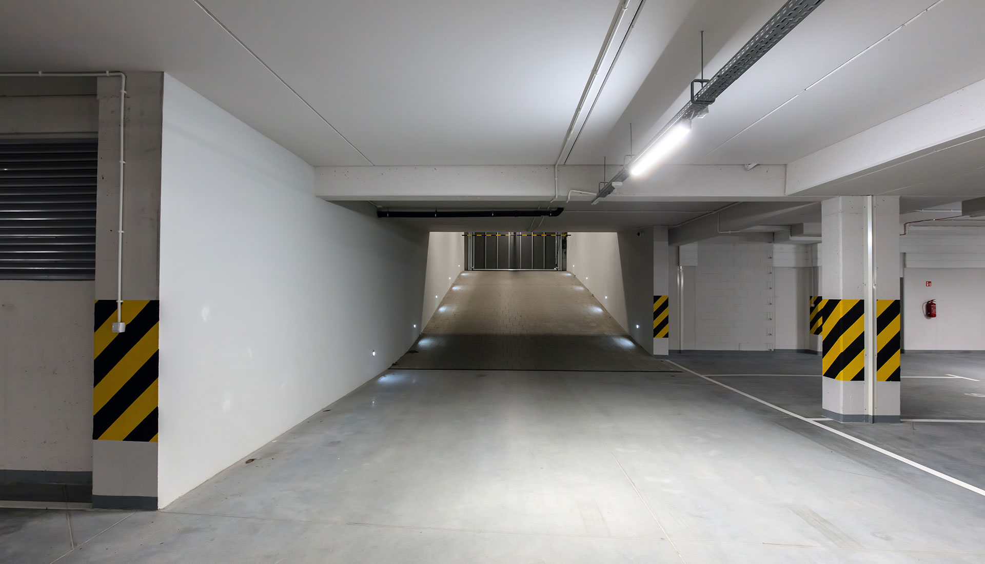frisch-renovierte-leere-garage-1 Moderne, gut beleuchtete Tiefgarage mit sauberen weißen Wänden und Warnmarkierungen an den Säulen